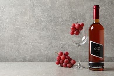 Photo of Bottle of delicious rose wine, glass and grapes on light grey table, space for text