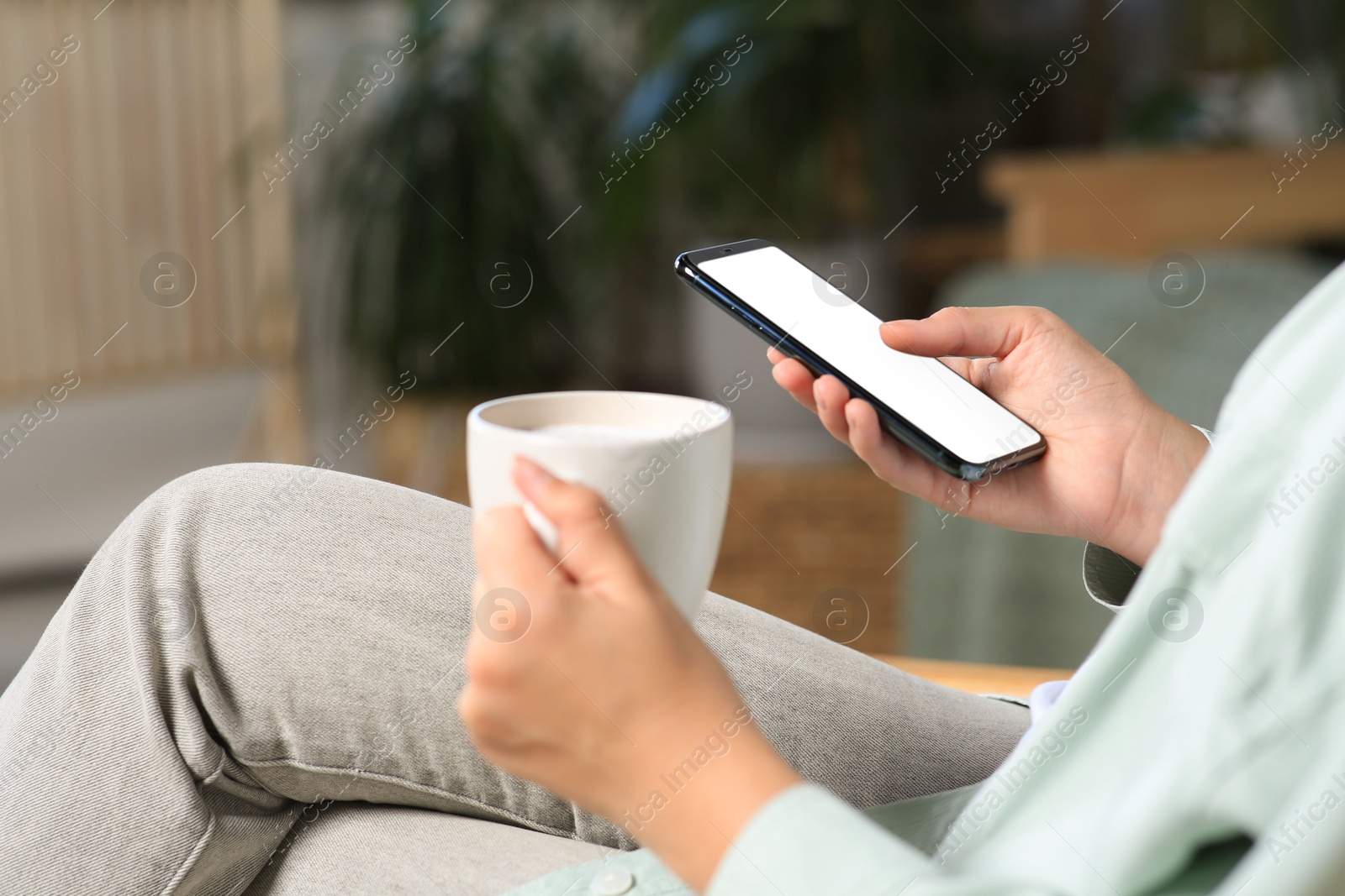 Photo of Woman with smartphone and cup of coffee indoors, closeup