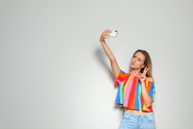 Beautiful woman taking selfie on light background