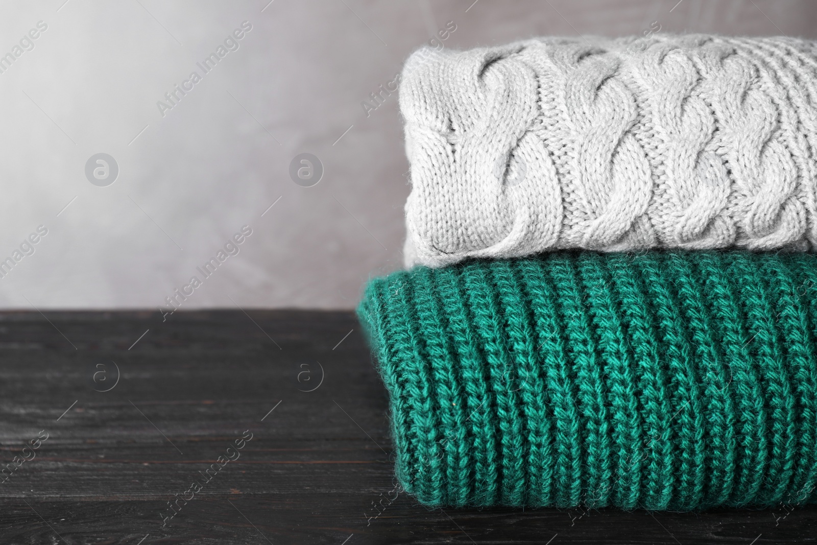 Image of Folded warm sweaters on black wooden table. Space for text