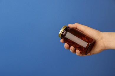 Photo of Woman holding jar with vitamin capsules on blue background, closeup. Space for text