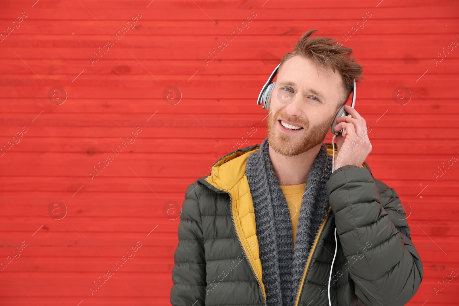 Photo of Young man listening to music with headphones against color wall. Space for text