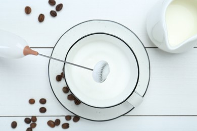 Flat lay composition with mini mixer (milk frother), whipped milk and coffee beans on white wooden table