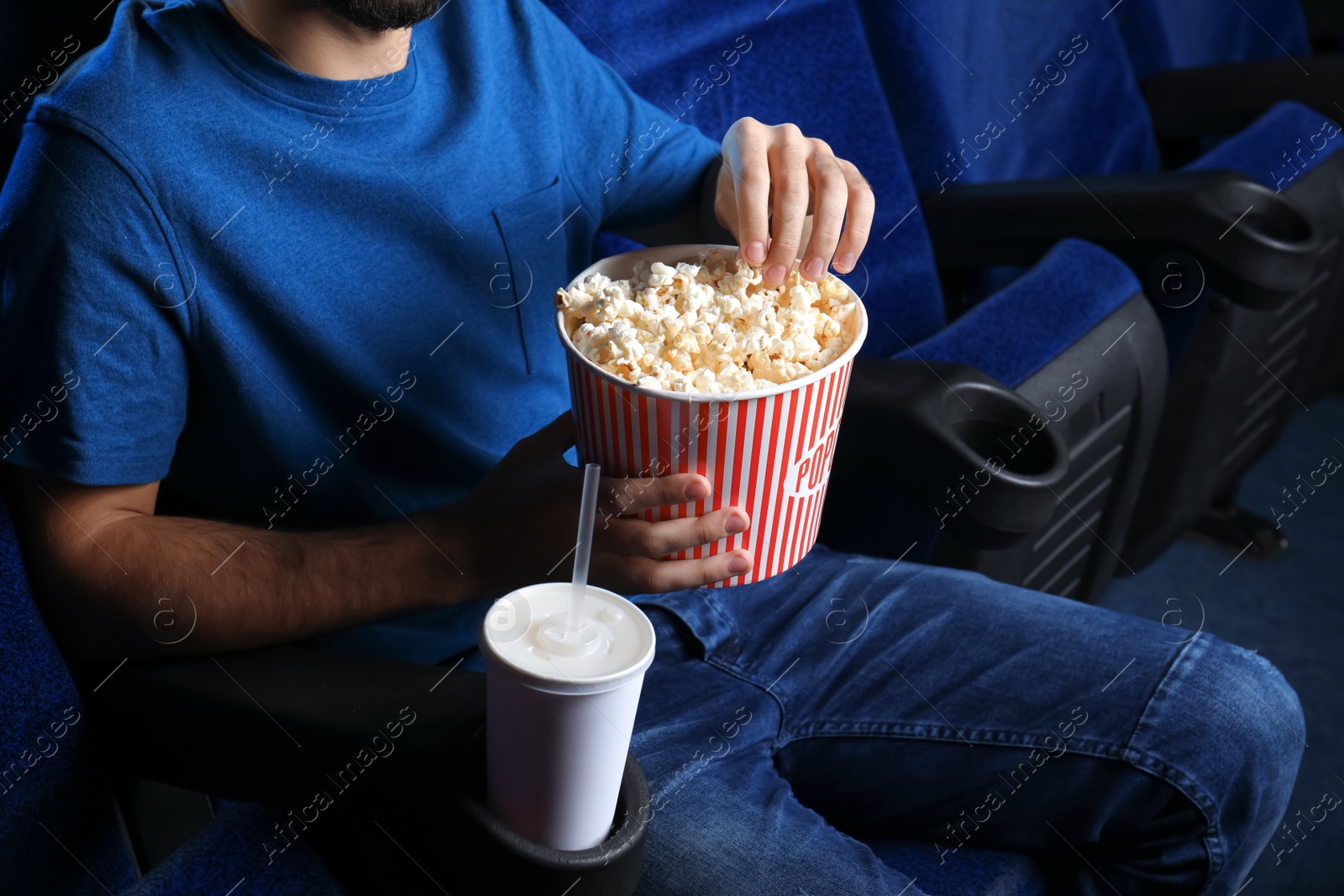 Photo of Young man with popcorn watching movie in cinema, closeup