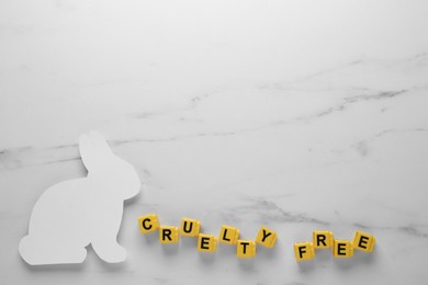 Photo of Flat lay of cubes with phrase Cruelty Free and rabbit figure on white marble table, space for text. Stop animal tests