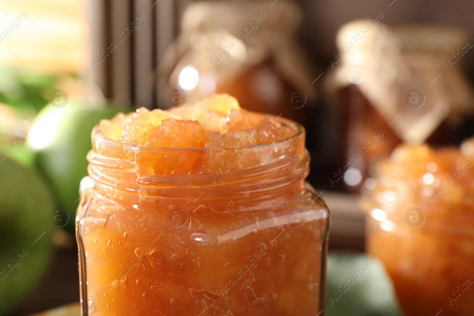 Photo of Glass jar of delicious apple jam against blurred background, closeup