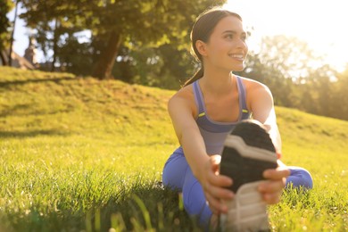 Attractive woman doing exercises on green grass in park, space for text. Stretching outdoors