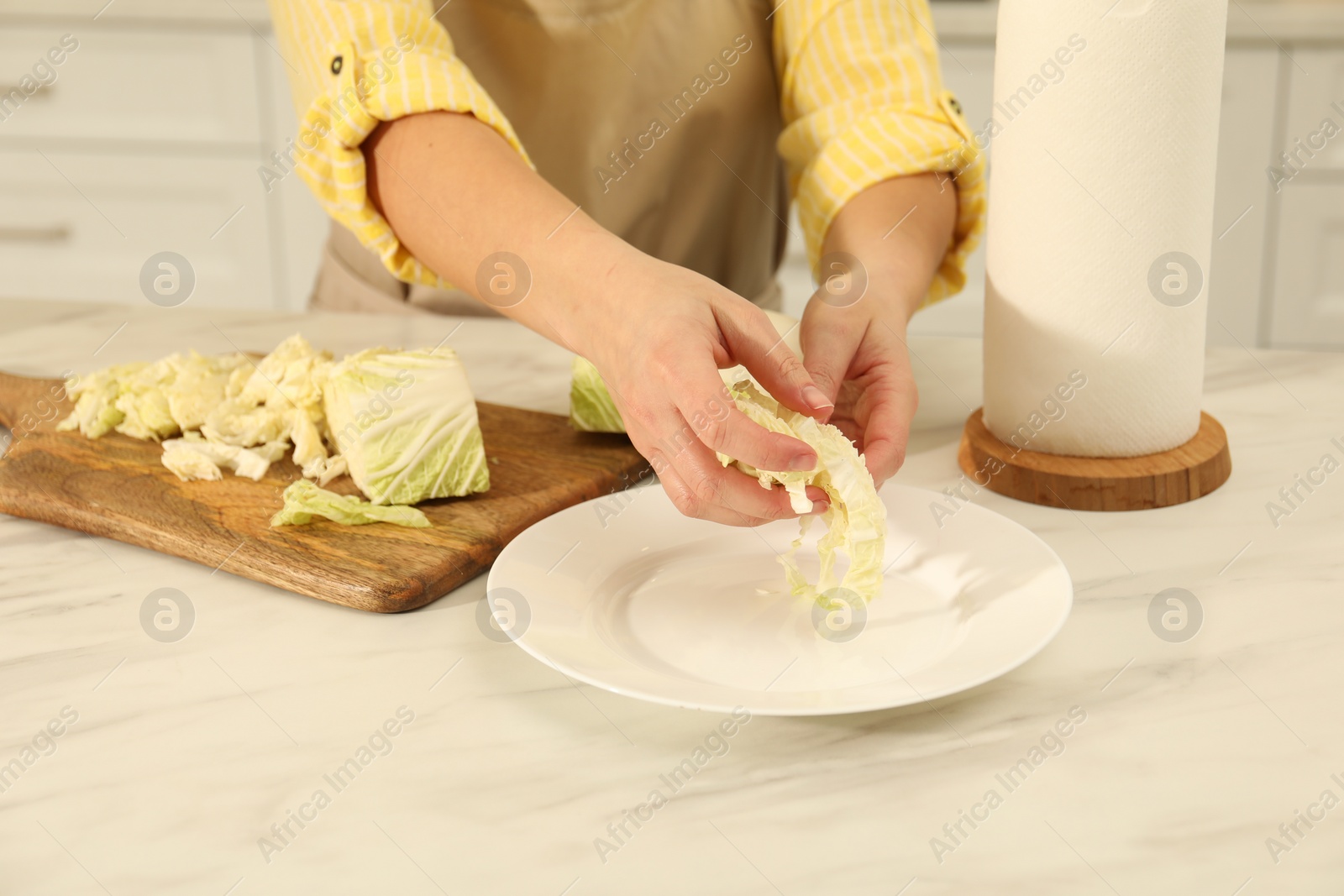 Photo of Woman putting cut Chinese cabbage into plate at white kitchen table, closeup