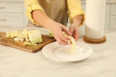 Photo of Woman putting cut Chinese cabbage into plate at white kitchen table, closeup