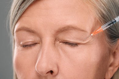 Senior woman getting facial injection on light grey background, closeup. Cosmetic surgery