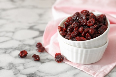 Photo of Dried cranberries in bowl on white marble table, space for text