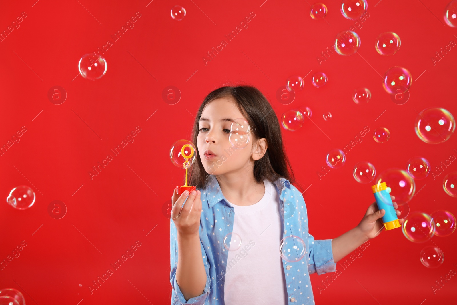 Photo of Little girl blowing soap bubbles on red background