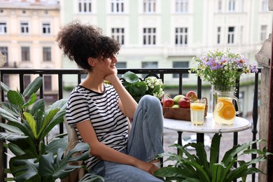 Young woman relaxing at table on balcony with beautiful houseplants