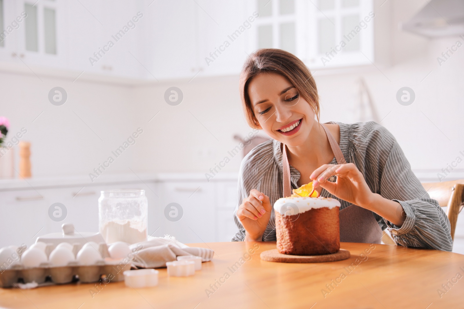 Photo of Young woman decorating traditional Easter cake in kitchen. Space for text