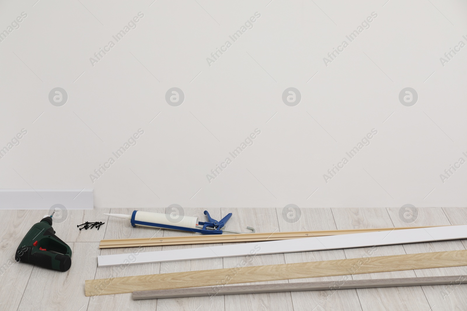 Photo of Plinths, caulking gun, screwdriver and screws on laminated floor in room