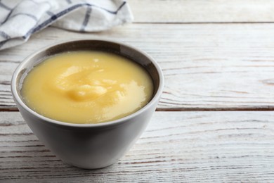 Photo of Bowl of Ghee butter on white wooden table, closeup. Space for text