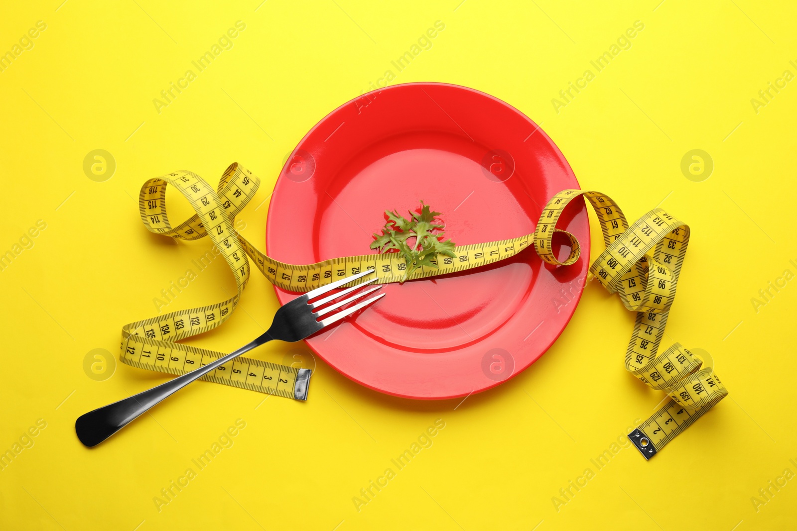 Photo of Plate with arugula, measuring tape and fork on yellow background, top view. Diet concept