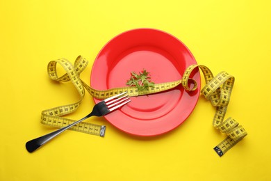 Plate with arugula, measuring tape and fork on yellow background, top view. Diet concept