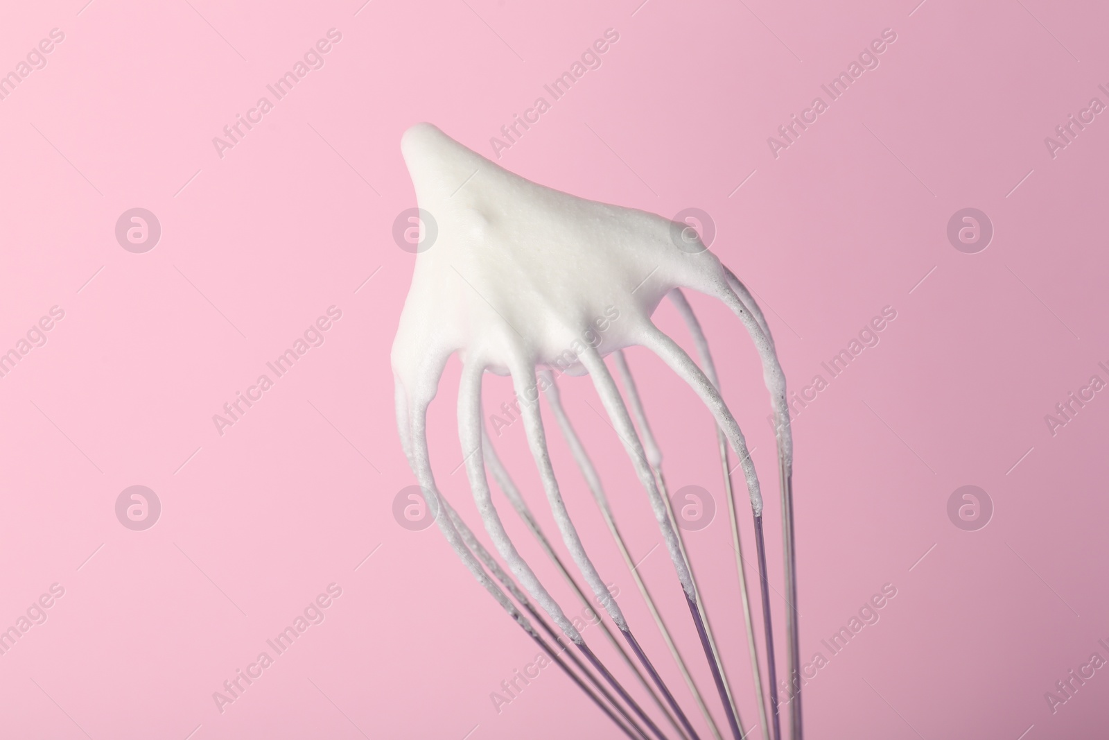 Photo of Whisk with whipped egg whites on pink background, closeup