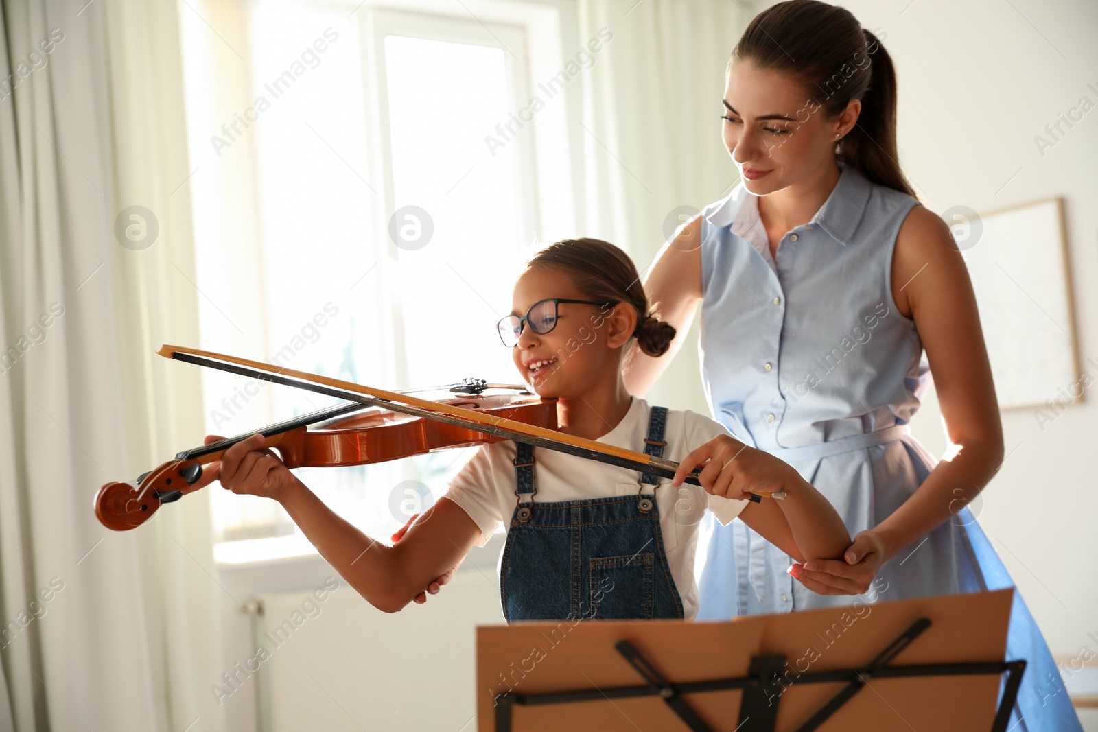 Photo of Young woman teaching little girl to play violin indoors