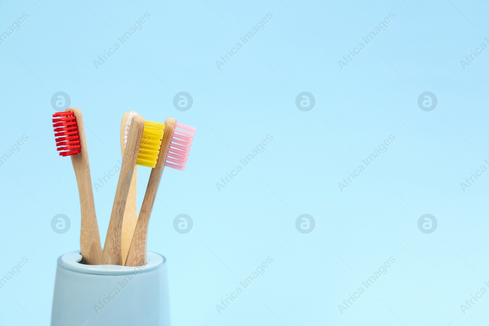 Photo of Toothbrushes made of bamboo in holder on light blue background. Space for text