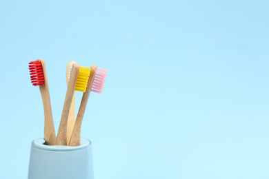Photo of Toothbrushes made of bamboo in holder on light blue background. Space for text