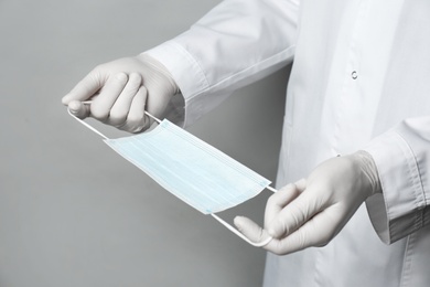 Photo of Doctor in medical gloves holding protective mask on light grey background, closeup