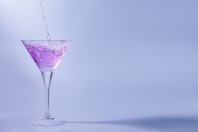 Pouring fresh cocktail into martini glass on light blue background, space for text