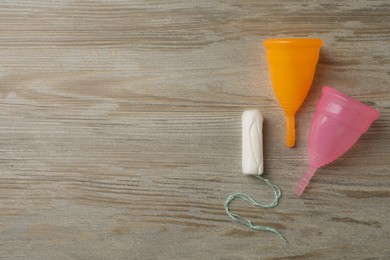 Menstrual cups and tampon on wooden background, flat lay. Space for text