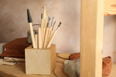 Photo of Clay and set of modeling tools on wooden table in workshop