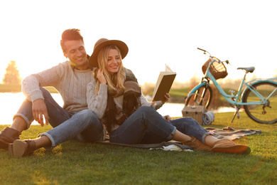 Photo of Happy young couple reading book while having picnic outdoors