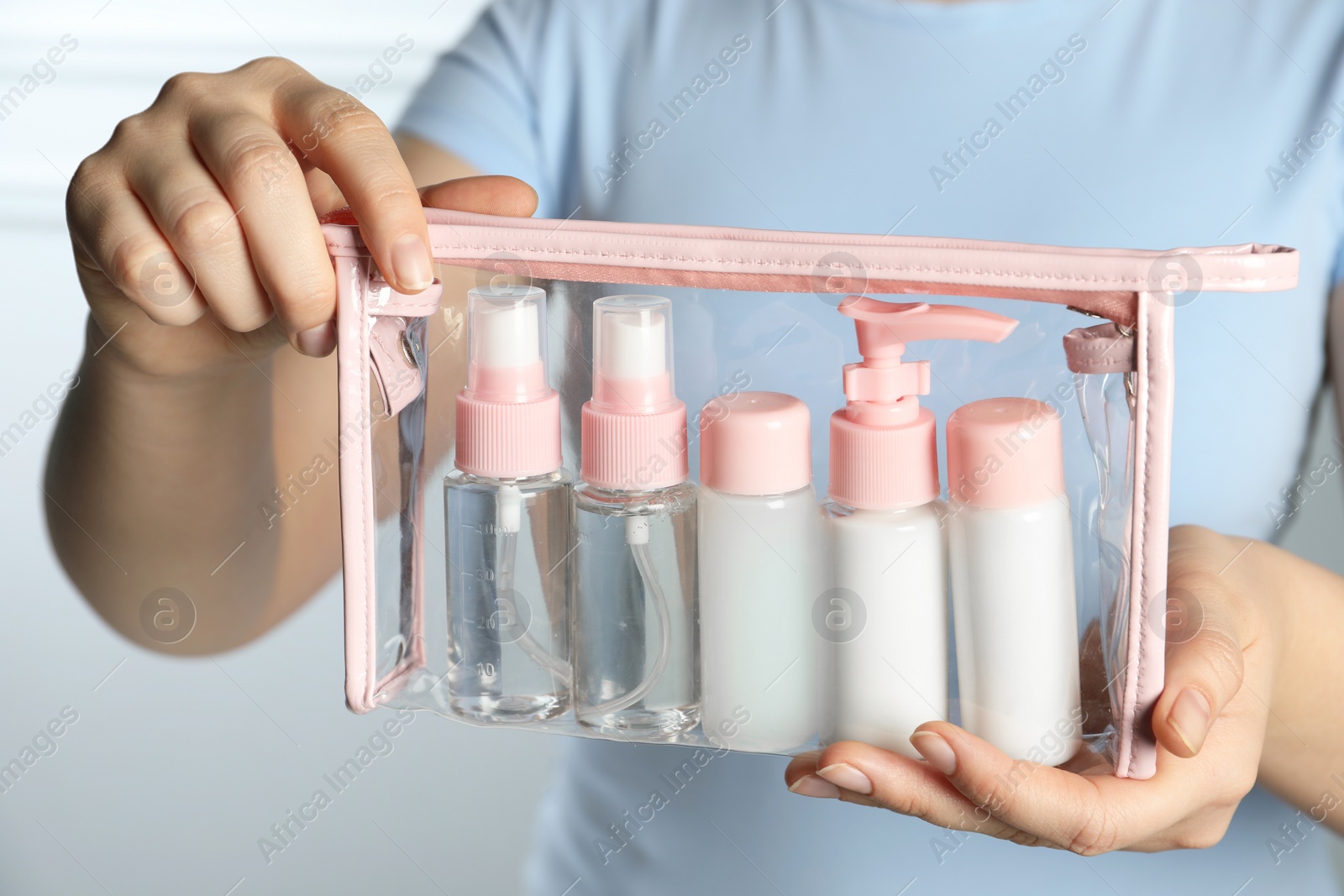 Photo of Woman with cosmetic travel kit on light background, closeup