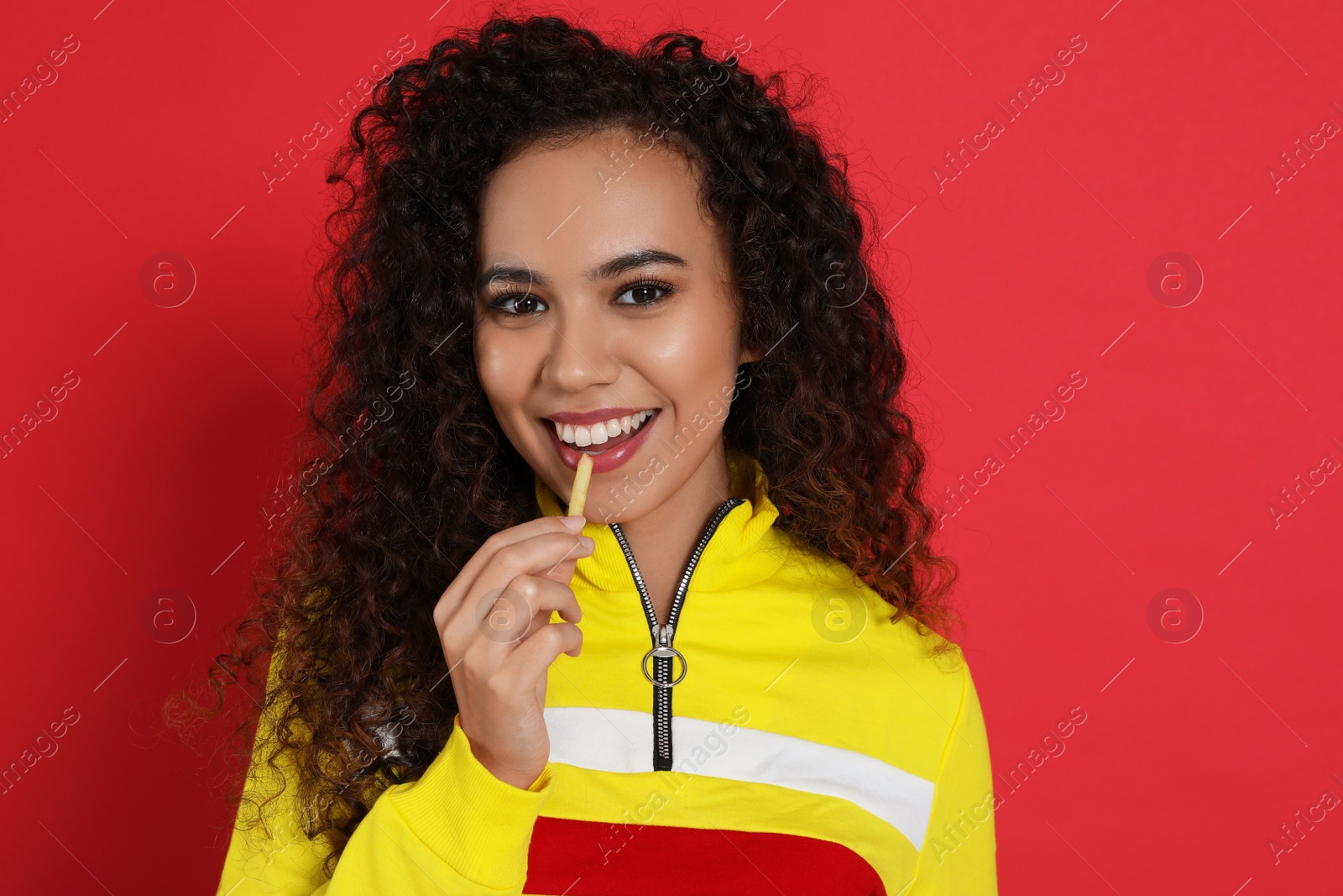 Photo of African American woman eating French fries on red background