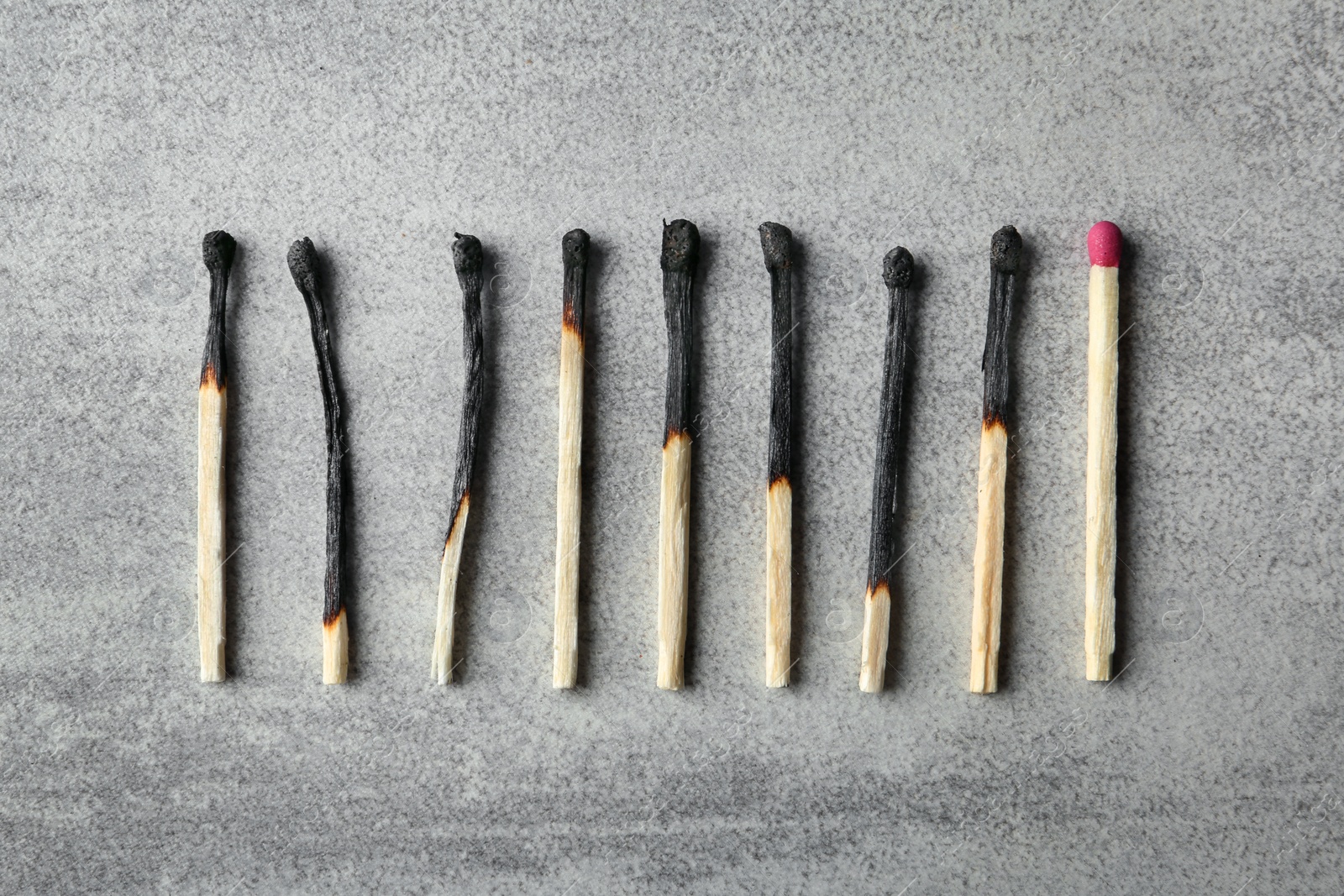 Photo of Row of burnt matches and whole one on grey background, flat lay. Uniqueness concept