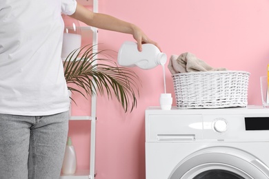 Photo of Woman pouring liquid detergent into cap on washing machine in laundry room, closeup