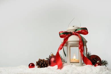 Decorative lantern and Christmas decor on snow against light grey background. Space for text