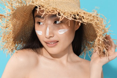 Photo of Beautiful young woman in straw hat with sun protection cream on her face against light blue background