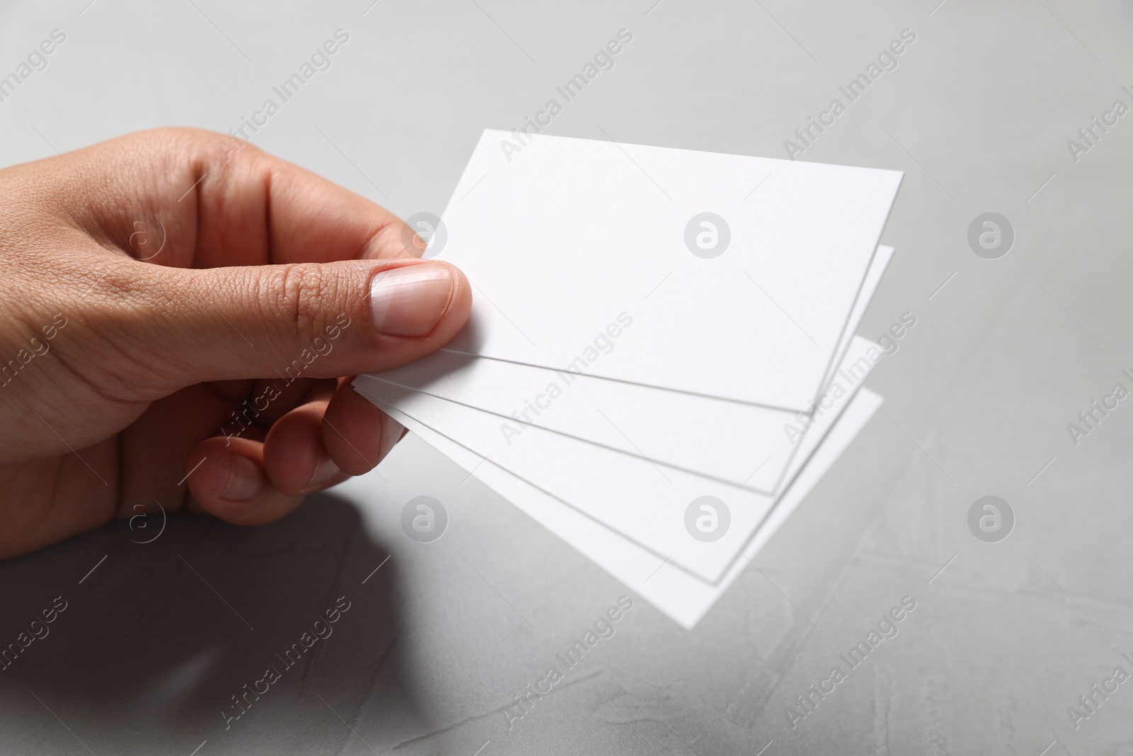 Photo of Man holding white blank cards at light grey table, closeup. Mockup for design