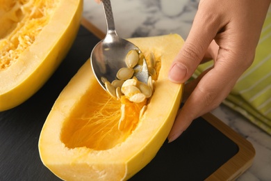 Photo of Woman removing seeds from spaghetti squash on table, closeup