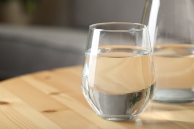 Jug and glass of water on wooden table in room, closeup with space for text. Refreshing drink
