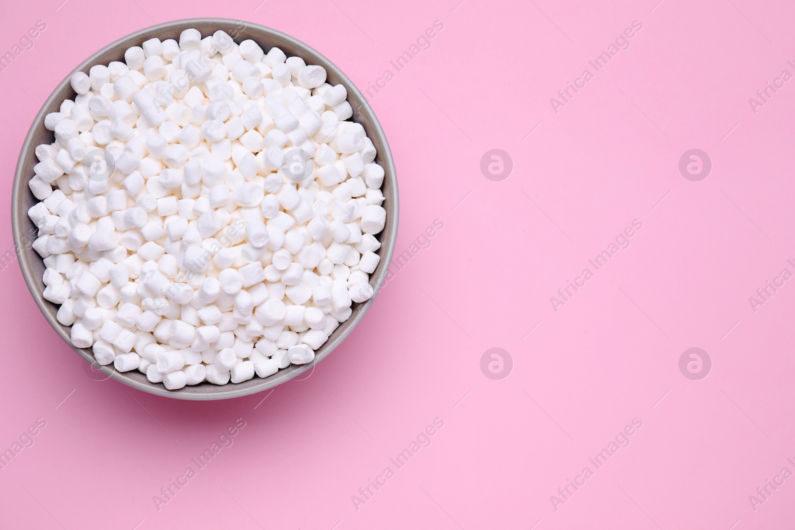 Photo of Bowl of sweet marshmallows on pink background, top view. Space for text