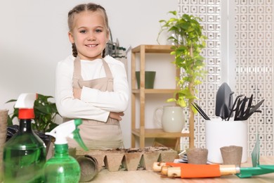 Photo of Little girl near garden tools on table indoors. Growing vegetable seeds