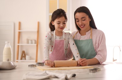 Photo of Mother with her cute little daughter rolling dough in kitchen