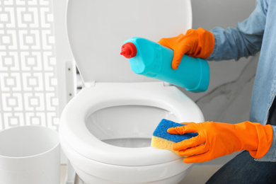 Woman cleaning toilet bowl in bathroom, closeup