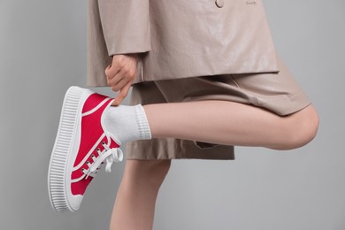 Photo of Woman putting on red classic old school sneaker against light gray background, closeup