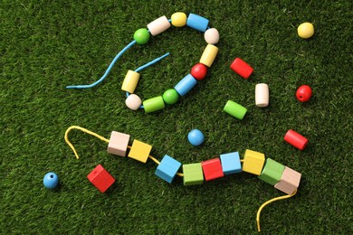 Photo of Wooden pieces and strings for threading activity on artificial grass, flat lay. Educational toy for motor skills development