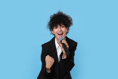 Beautiful young woman with microphone singing on light blue background
