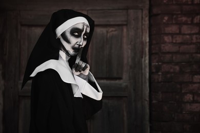 Photo of Portrait of scary devilish nun near red brick wall, space for text. Halloween party look
