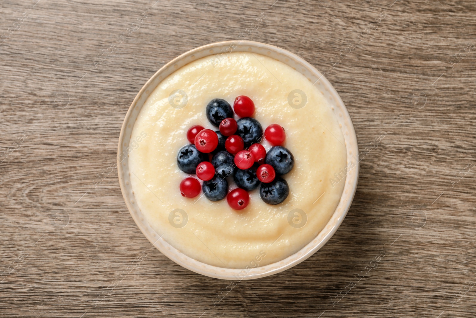 Photo of Delicious semolina pudding with berries on wooden table, top view