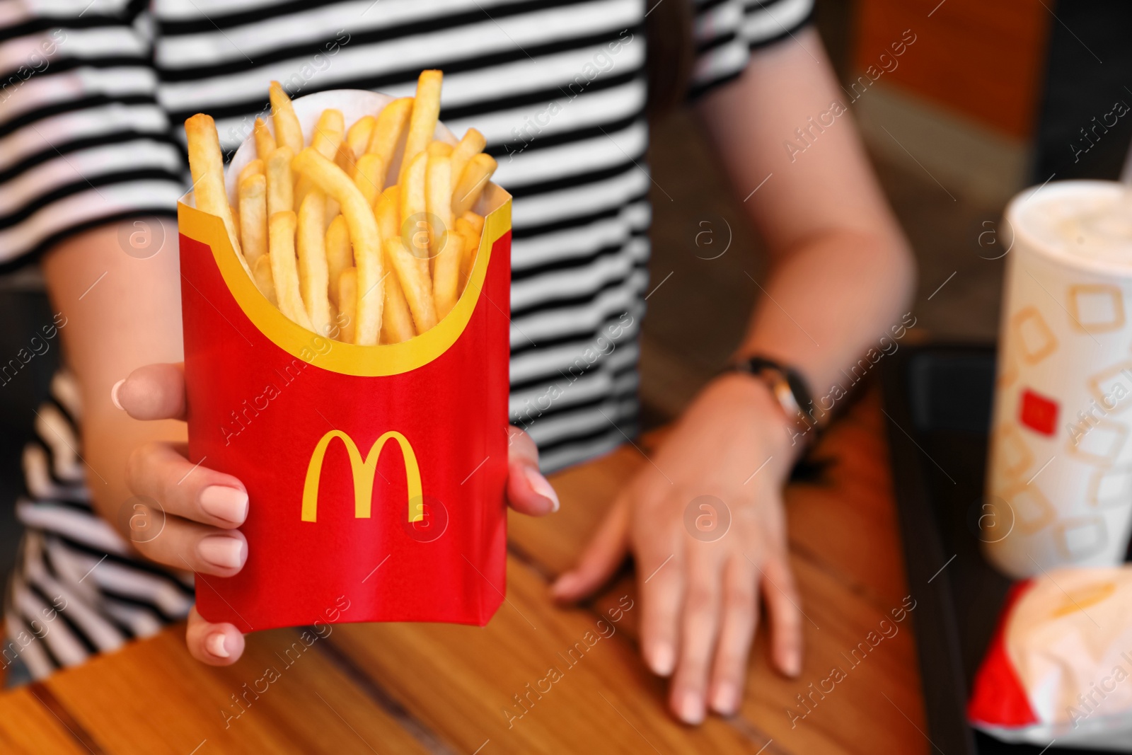 Photo of MYKOLAIV, UKRAINE - AUGUST 11, 2021: Woman with McDonald's French fries and drink at table in cafe, closeup